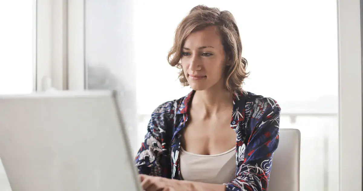 Young woman with short hair working on a laptop in a bright, modern home office environment, focused on her work.